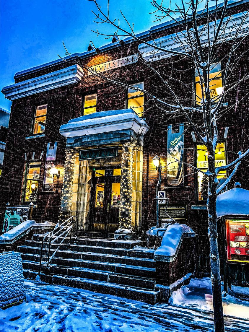 Revelstoke Museum & Archives front entrance. with wet snow collecting and falling from the sky. It is early evening and the lights are bright.