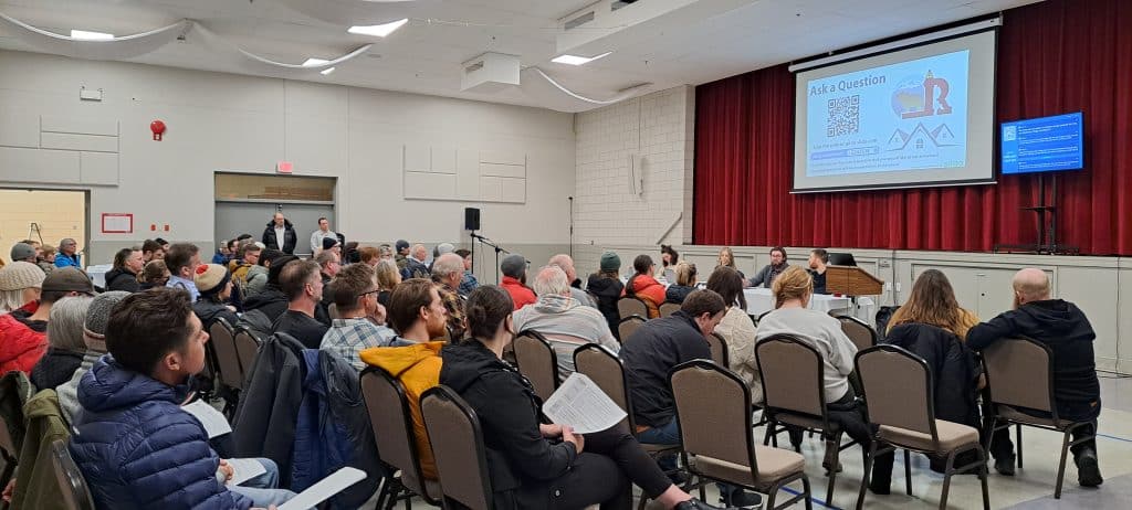 Revelstoke residents sitting in a gym watching a presentation for STR regulations in the city and the province.