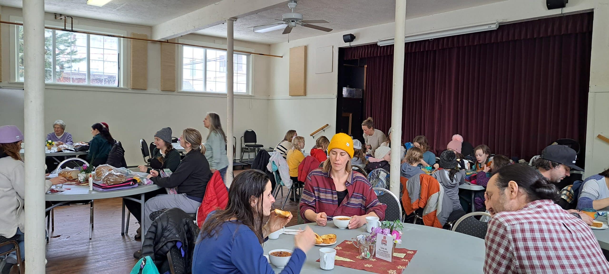 A hall filled with Revelstoke residents sitting and standing as they enjoy Soup and a Smile