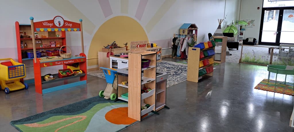 Ray of Sunshine daycare main play area with two drama centres on the left hand side. One stylized as a grocery store and one as a nature section with toy animals.