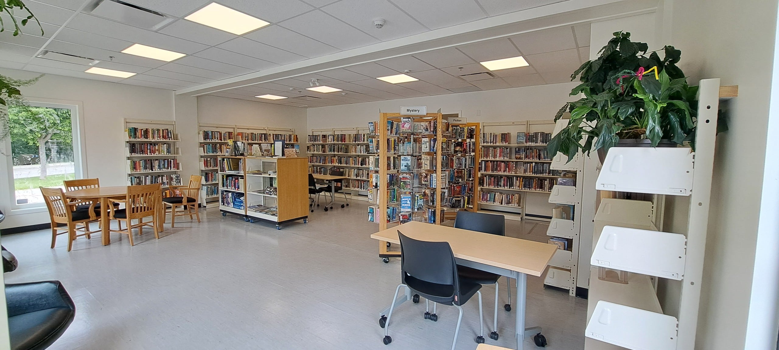 Revelstoke library new space with multiple shelves of books, white tile, a collection of desks and chairs and large windows.