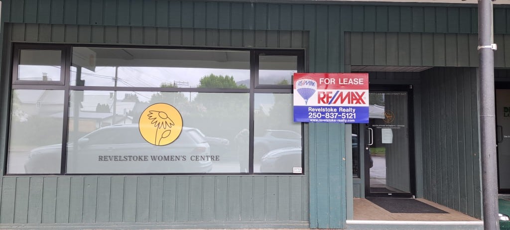 Front entrance of the Revelstoke Women's Centre with a re/max for sale sign posted beside a large window with the women's centre logo still in it.