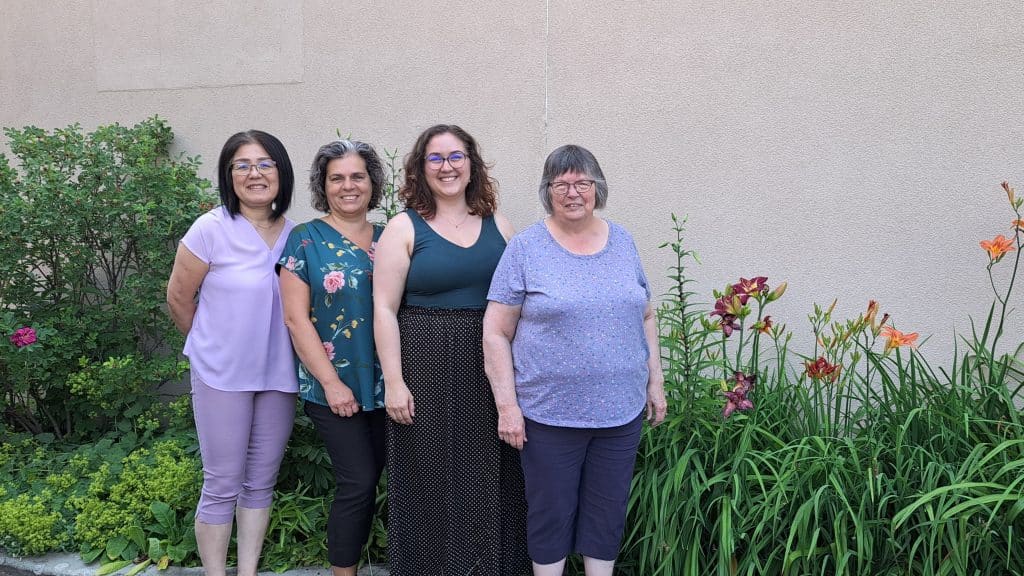 Four women standing in a garden smiling at a camera