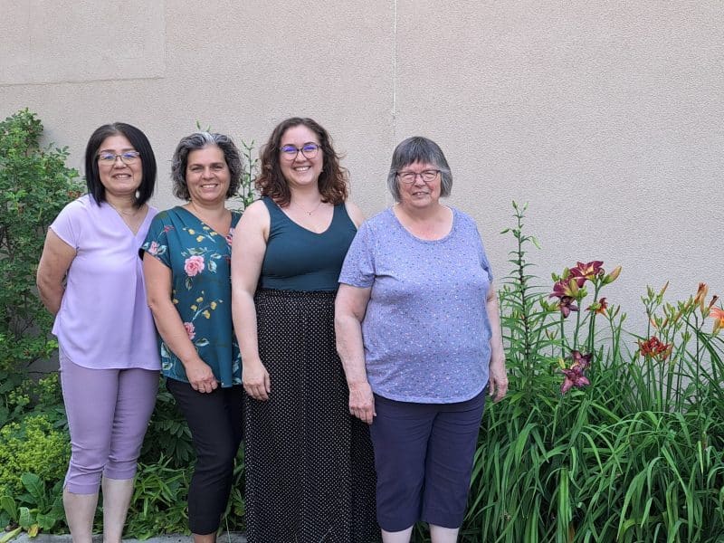 Four women standing in a garden smiling at a camera