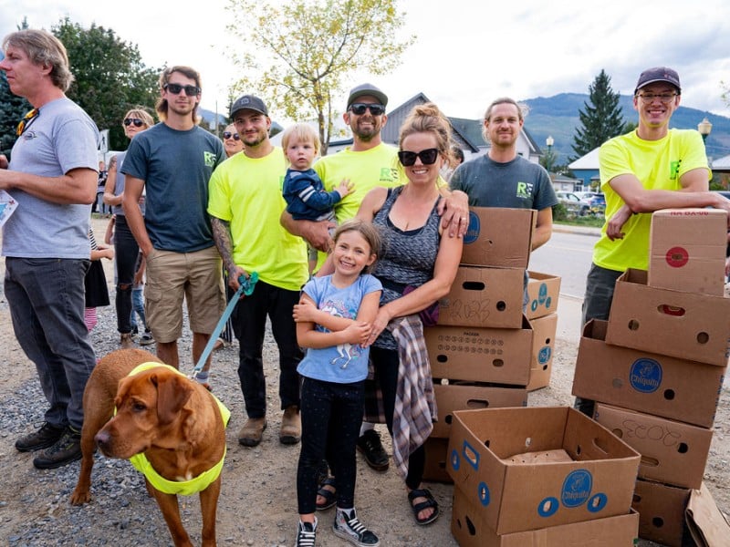 A collection of volunteers standing around boxes filled with food donations under a large white tent.