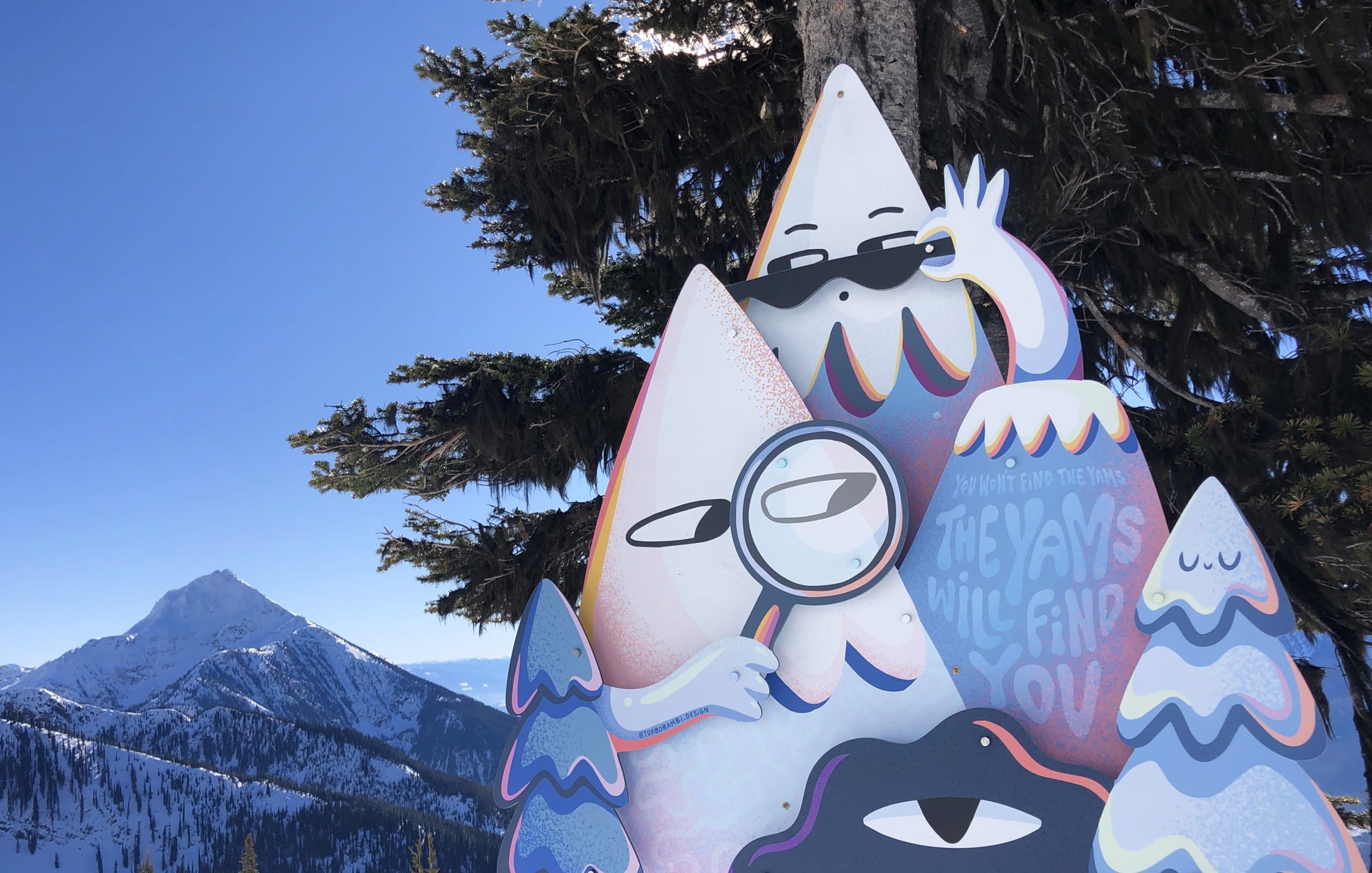 ROAM art installation The Yams Will Find You by local artist Turbo Bambi featuring two mountains and a hill all with eyes scoping out the local hill. One Mountain is wearing a pair of sunglasses, one is holding up a microscope.