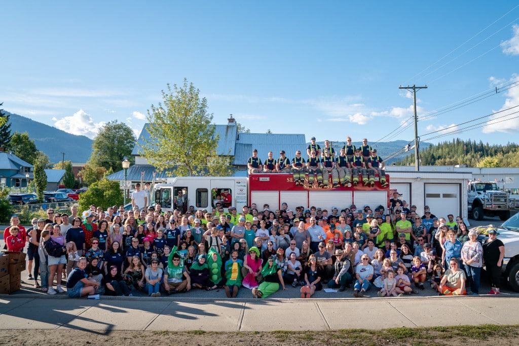 a large gathering of volunteers, roughly 200 stand in front of a firetruck as they cheer for the emergency services food drive