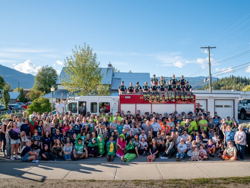 a large gathering of volunteers, roughly 200 stand in front of a firetruck as they cheer for the emergency services food drive