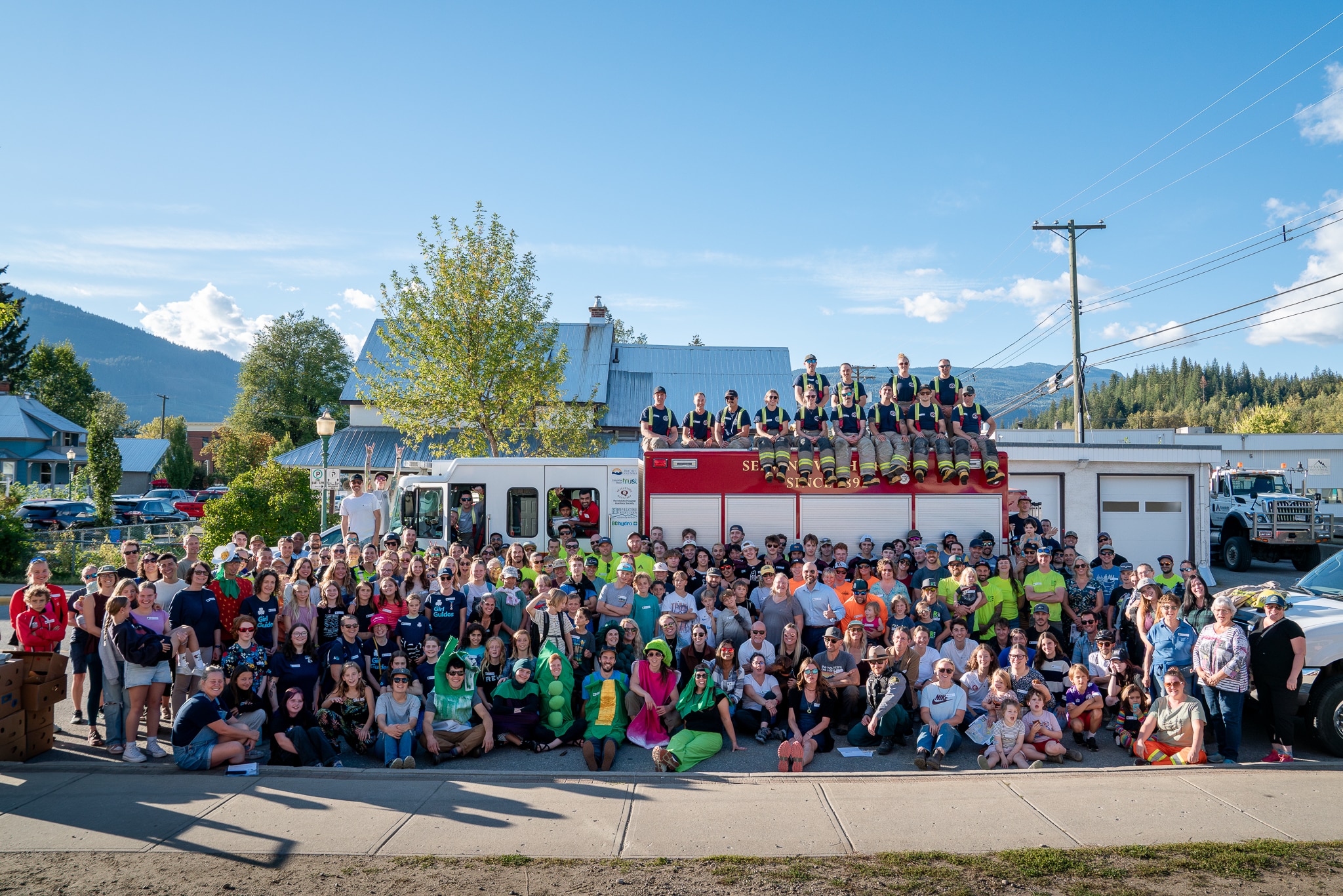 a large gathering of volunteers, roughly 200 stand in front of a firetruck as they cheer for the emergency services food drive